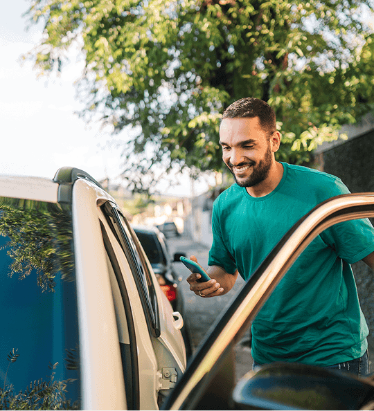 A man in a teal shirt smiles while leaning into a car window.