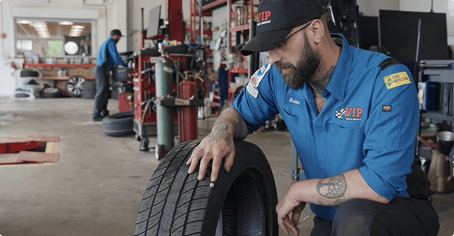 Mechanic in blue uniform inspects a car tire in an automotive repair shop.