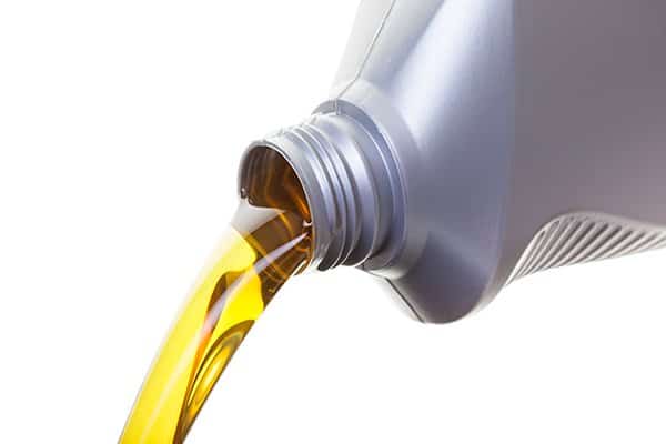 Golden motor oil pours from a tilted silver bottle.