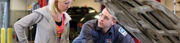 Two workers in hard hats and safety gear discuss plans in an industrial workshop setting.