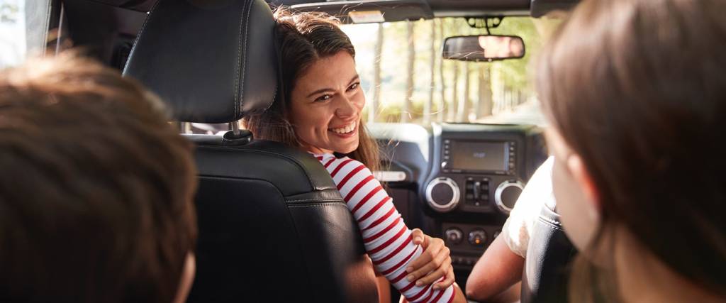 A woman in a red and white striped shirt smiles while sitting in the driver's seat of a car.