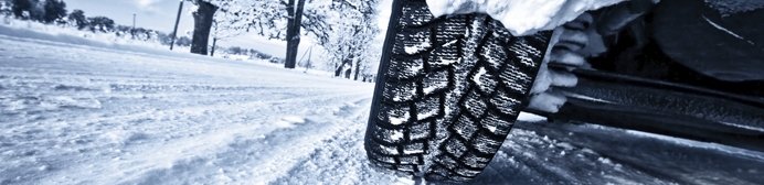 A winter tire with deep treads grips a snowy road surface.