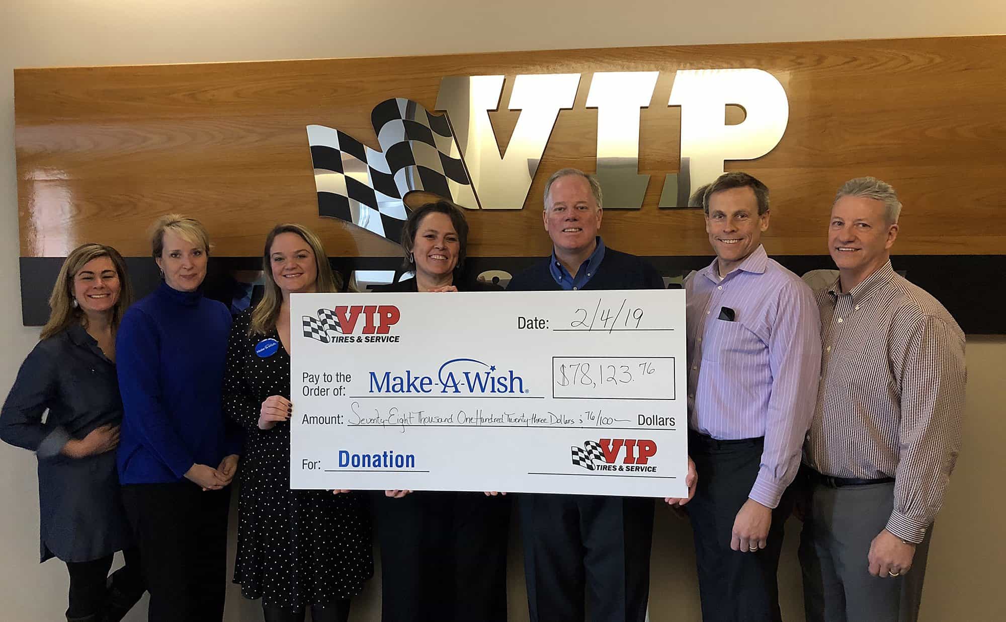 Seven people hold a large donation check from VIP Tire & Service to Make-A-Wish Foundation.