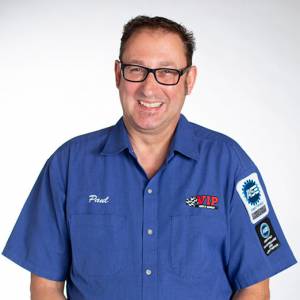 Man wearing blue work shirt with name tag and patches, smiling at camera.