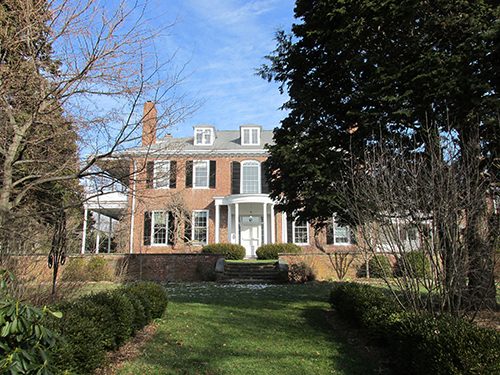 A brick colonial-style house with white columns and shutters, viewed from the front lawn.