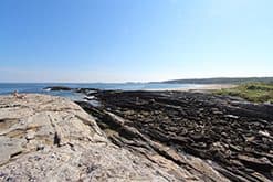 A rocky black lava field stretches toward the ocean under a clear blue sky.