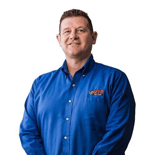 A man wearing a blue button-up shirt with an embroidered logo stands against a white background.