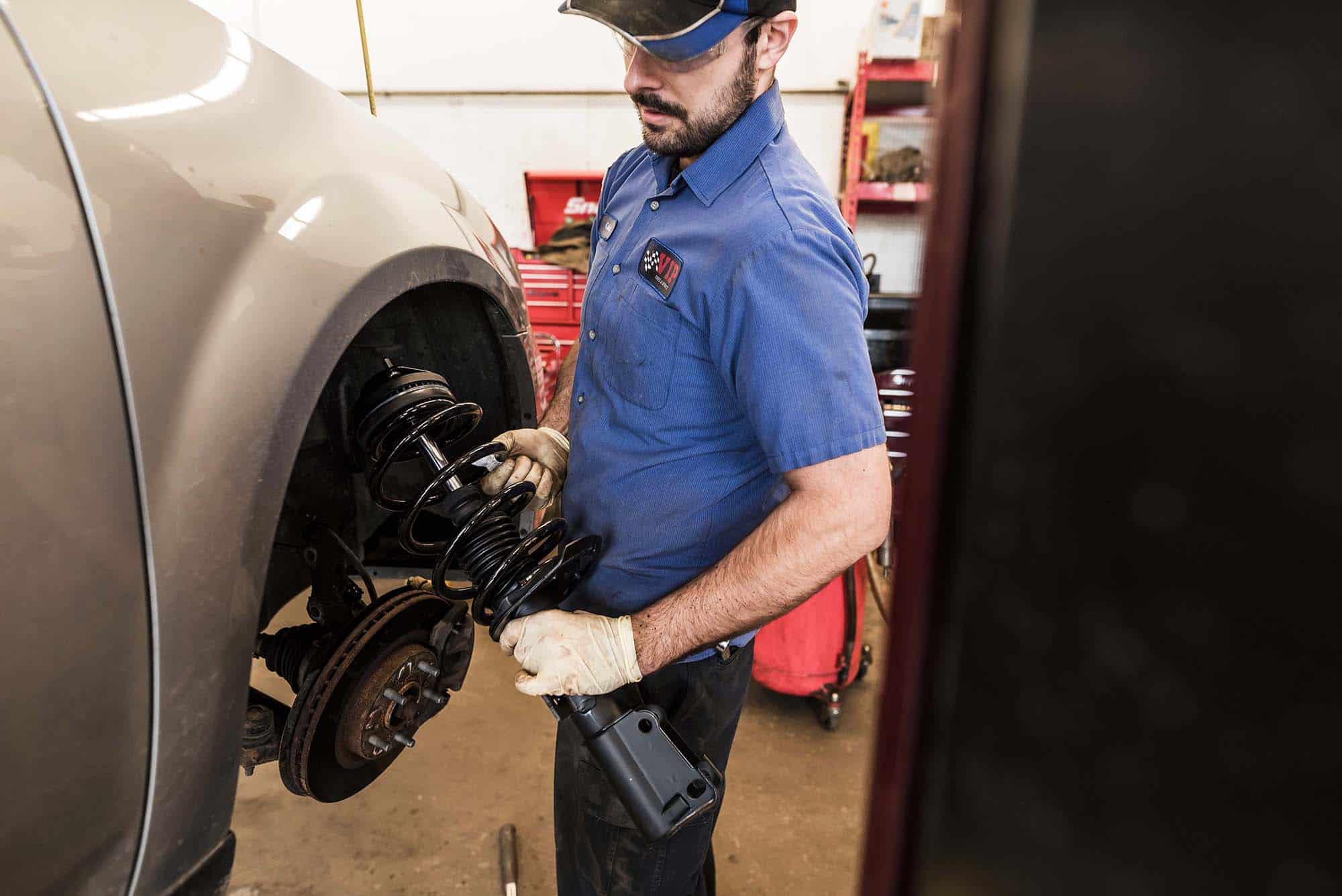 Mechanic in blue shirt and cap inspects a vehicle's brake assembly in a garage.