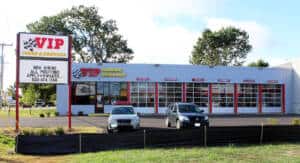 VIP auto dealership storefront with red-trimmed windows, two parked vehicles, and a hiring sign.