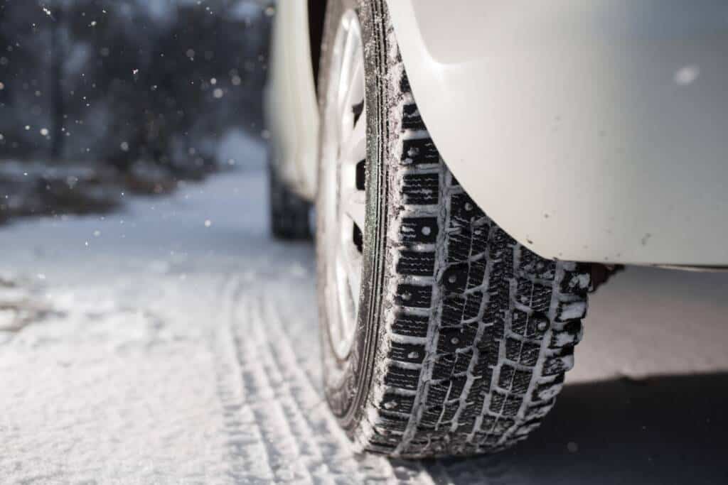 Close-up of a winter tire with deep tread on a snow-covered road.