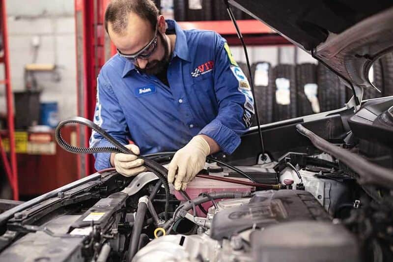 VIP automotive professional removing a timing belt from the hood of a car.