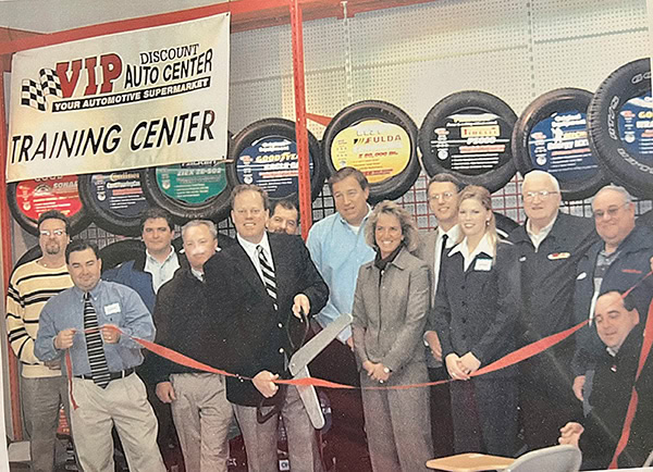 Group of people cutting a red ribbon at a VIP Auto Center Training Center opening ceremony.