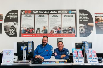 Two mechanics in blue uniforms stand behind a counter at an auto service center.