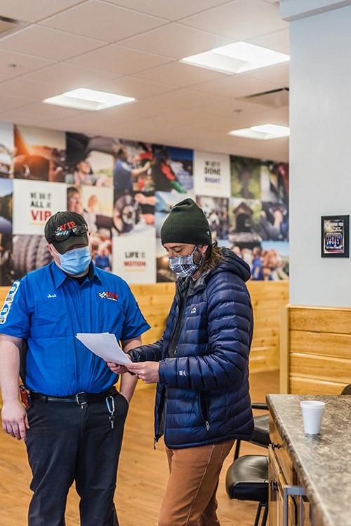 A person in a blue uniform and mask hands a document to another person wearing a dark jacket.