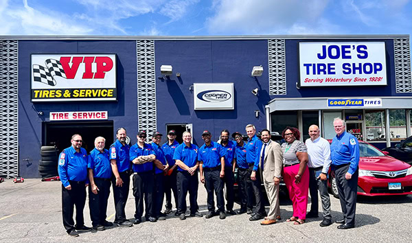A group of people in blue shirts stand outside Joe's Tire Shop storefront.