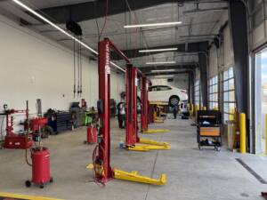 Modern automotive repair shop with red hydraulic lifts and a white car elevated on one lift.