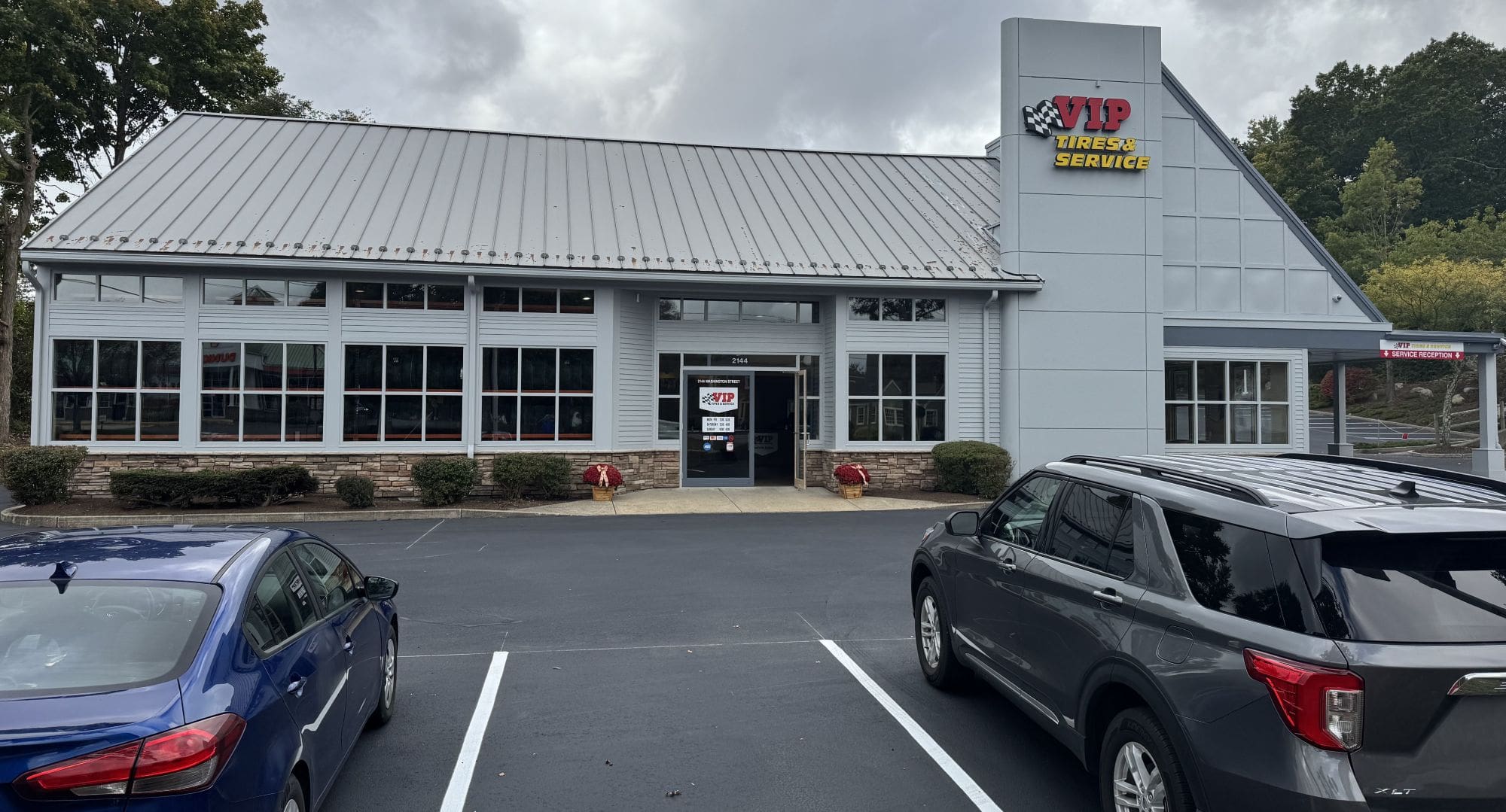 A white building with metal roof and large windows displays an automotive service sign in its.